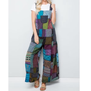 Może przedstawiać: Kombinezon patchwork w różnych kolorach, w tym niebieskim, fioletowym, zielonym i brązowym. Kombinezon z szerokimi nogawkami ma kieszeń na piersi i regulowane ramiączka. Ubranie wykonane jest z różnych kwadratów materiału.
