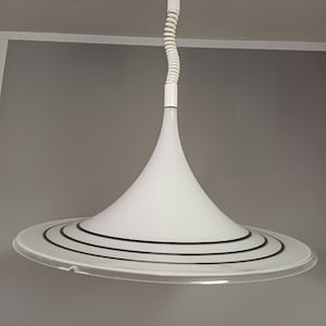May include: White pendant light with a white, coiled cord and a white, cone-shaped shade with a black, concentric ring design.