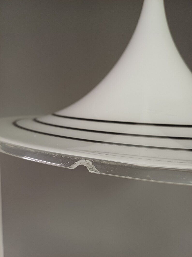 May include: A white glass lampshade with a wide, circular base and three black bands around the rim. The base is slightly chipped.