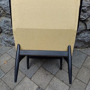 K&ouml;nnte beinhalten: Ein schwarzer Holzstuhl mit einem beigen Stoffbezug f&uuml;r Sitzfl&auml;che und R&uuml;ckenlehne. Der Stuhl hat ein einzigartiges Design mit abgewinkelten Beinen.