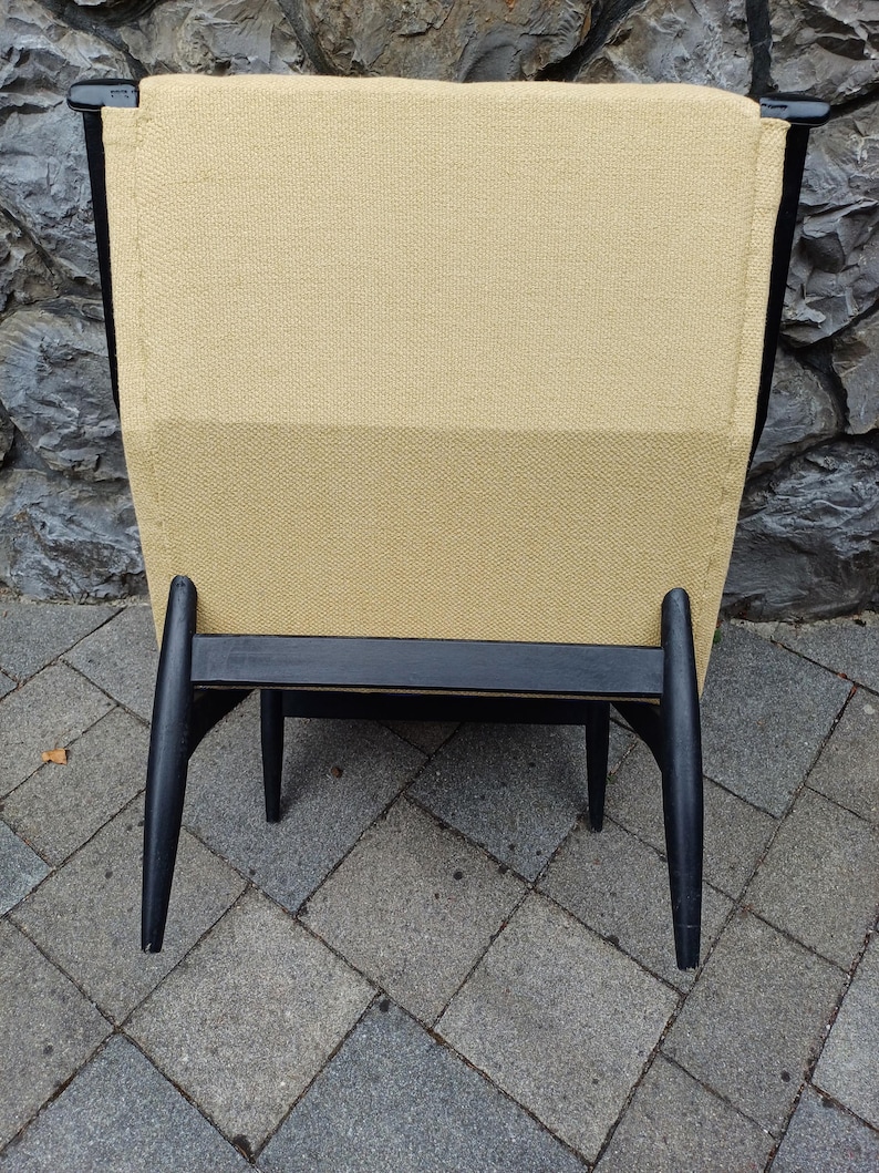 K&ouml;nnte beinhalten: Ein schwarzer Holzstuhl mit einem beigen Stoffbezug f&uuml;r Sitzfl&auml;che und R&uuml;ckenlehne. Der Stuhl hat ein einzigartiges Design mit abgewinkelten Beinen.