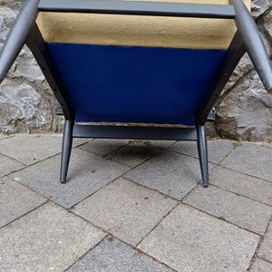 K&ouml;nnte beinhalten: Ein schwarzer Holzstuhl mit einem blauen Stoffbezug und einer beigefarbenen Stofflehne.