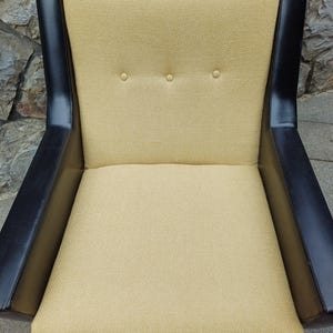 K&ouml;nnte beinhalten: Ein gelber Sessel mit schwarzem Lederbesatz. Der Sessel hat eine gesteppte R&uuml;ckenlehne und einen gesteppten Sitz.
