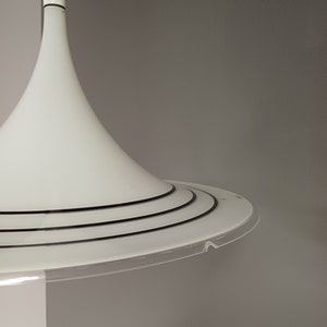 May include: White pendant light with a wide, circular base and a narrow, cone-shaped shade. The base has three black rings around the edge.