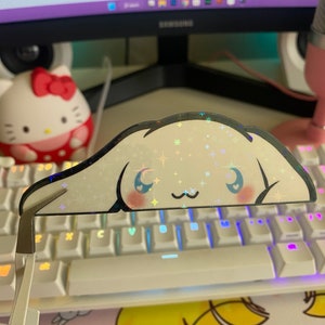 May include: A holographic iridescent sticker of a cartoon dog with a white background and glitter accents. The sticker is placed on a white keyboard with rainbow backlighting.