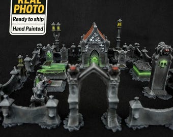 Puede incluir: Diorama de cementerio en miniatura pintado a mano con una capilla central, lápidas y un muro circundante. La escena presenta acentos verdes brillantes y está ambientada sobre un fondo oscuro. La imagen incluye una pegatina "REAL PHOTO".