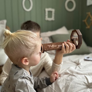 May include: A wooden kaleidoscope with a white background and the words "Follow you" printed on it. The kaleidoscope is being held by a child.
