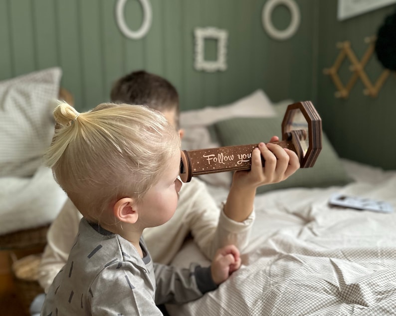 May include: A wooden kaleidoscope with a white background and the words "Follow you" printed on it. The kaleidoscope is being held by a child.