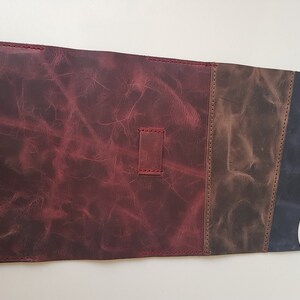 May include: A rectangular leather roll-up case featuring a large deep red section, a smaller brown panel, and a dark blue flap. The leather has a distressed texture with visible stitching and a small metal stud closure on the flap.