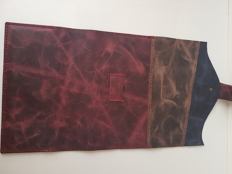 May include: A rectangular leather roll-up case featuring a large deep red section, a smaller brown panel, and a dark blue flap. The leather has a distressed texture with visible stitching and a small metal stud closure on the flap.