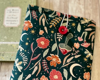 May include: A dark green fabric book cover with a floral pattern featuring red, pink, and white flowers, leaves, and a crescent moon. The fabric has a subtle gold glitter throughout. A red button is attached to the cover.