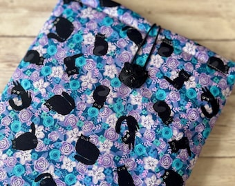 Pode incluir: Uma bolsa de tecido azul e roxo com estampa de gato preto e um tassel preto. A bolsa é forrada com um material macio e felpudo e é perfeita para guardar pequenos objetos.