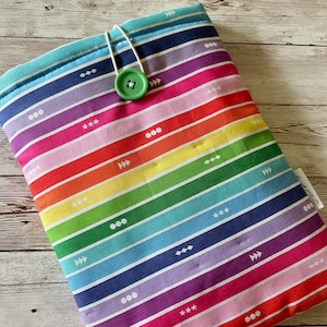 May include: A rainbow striped fabric book cover with a white button and a white string closure.