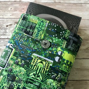 May include: A green and yellow book cover with a circuit board pattern. The cover has a black button in the center.