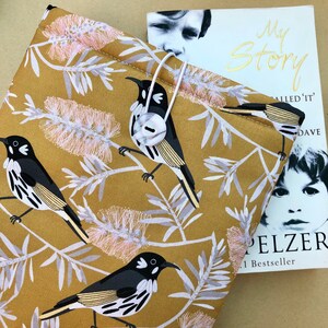 May include: A mustard yellow book cover with a white button closure. The cover features a repeating pattern of black and white birds and pink and white flowers. The text "My Story" is printed in gold on the cover.