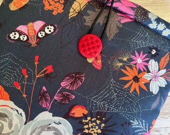 May include: A dark blue fabric pouch with a floral pattern featuring butterflies, spiders, and leaves. The pouch has a red button closure and a black elastic drawstring.
