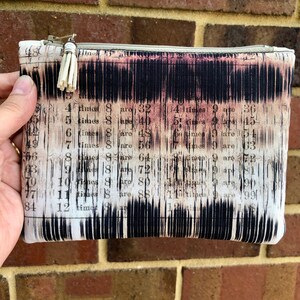 May include: A rectangular zipped pouch with a distinctive multiplication table print. The fabric has a vintage aesthetic with black, white, and pink tones. A small, cream-coloured tassel hangs from the zip pull.