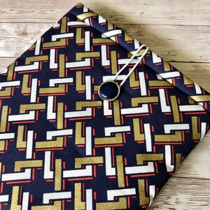 May include: A navy blue fabric case with a geometric pattern in gold, white, and red. The case has a decorative button closure.