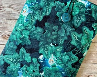 May include: A green and teal book sleeve featuring a pattern of ivy leaves. The sleeve has a button closure with a teal button and a black cord. The label "Frednpolly" is visible on the front.