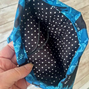 Puede incluir: Una bolsa de tela azul con un forro estampado en blanco y negro. La bolsa tiene un cord&oacute;n de ajuste negro y presenta un dise&ntilde;o de gato negro.