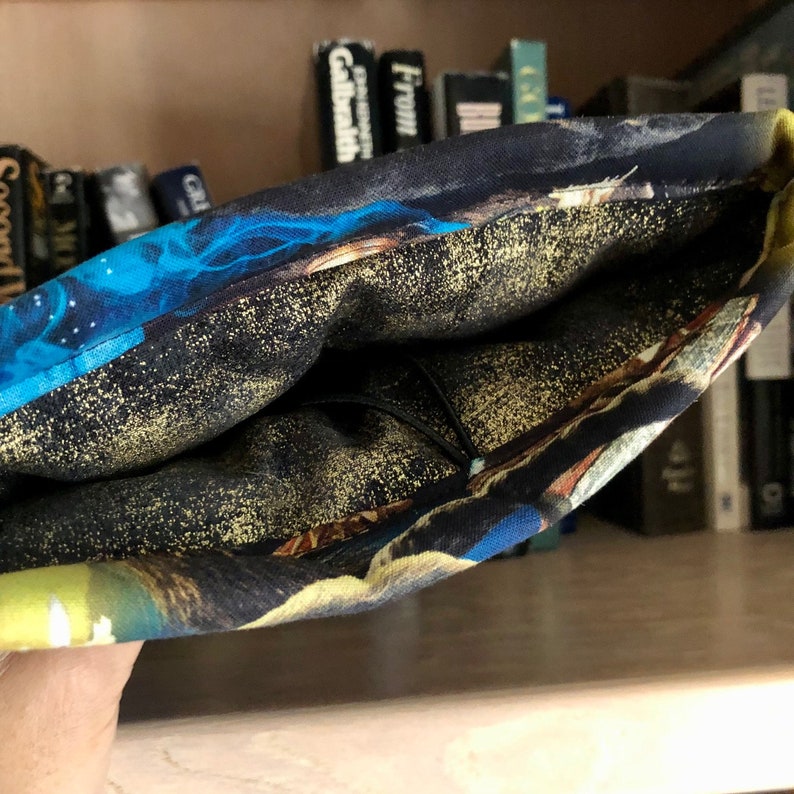 Op de afbeelding: Een zwarte en blauwe stoffen tas met een galaxy print en gouden glitter. De tas is binnenstebuiten gekeerd om de voering te laten zien.