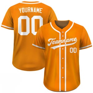 Pode incluir: Camisola de baseball laranja com detalhes brancos. A frente exibe "Teamname" e o n&uacute;mero "00". A parte de tr&aacute;s mostra "YOURNAME" e o n&uacute;mero "00". A camisola tem bot&otilde;es e mangas curtas.