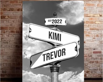 Könnte beinhalten: Schwarzweißes Bild von zwei Straßenschildern mit den Namen "Kimi" und "Trevor" darauf. Die Schilder sind an einem Metallpfosten befestigt, über dem ein kleineres Schild mit der Aufschrift "EST 2022" angebracht ist.