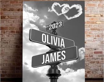 Op de afbeelding: Een zwart-wit straatnaambord met de namen "Olivia" en "James" erop. Het bord is bevestigd aan een paal met een hartvormige wolk erboven. Het bord heeft ook de tekst "EST. 2023" erop.