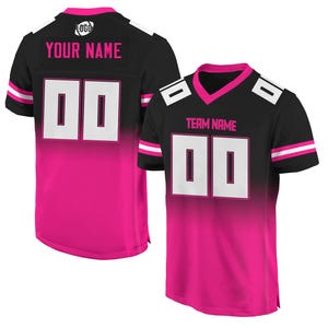May include: Black and pink football jersey with white accents. The jersey has a gradient design with a black top and pink bottom. The jersey has a white number "00" on the front and back. The jersey has the text "TEAM NAME" on the front and "YOUR NAME" on the back.