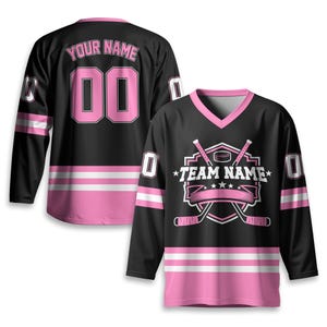 May include: Black hockey jersey with pink accents, featuring a V-neck and long sleeves. The jersey displays the text "TEAM NAME" and "YOUR NAME" with the number "00". Pink and white stripes adorn the sleeves and bottom hem.