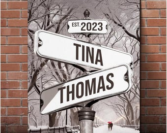 Op de afbeelding: Een zwart-witafbeelding van een straatnaambord met de tekst "EST. 2023" op het bovenste bord, "TINA" op het middelste bord en "THOMAS" op het onderste bord. De straatnaamborden bevinden zich in een besneeuwde winterse scène.