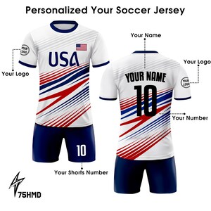 Puede incluir: Una camiseta de f&uacute;tbol blanca con rayas rojas y azules, con la palabra "USA" y una peque&ntilde;a bandera estadounidense en la parte delantera. La parte posterior de la camiseta tiene un fondo blanco con rayas rojas y azules y un n&uacute;mero negro "10" y el texto "YOUR NAME". La camiseta se combina con pantalones cortos azul marino con un n&uacute;mero blanco "10" en la pierna derecha.