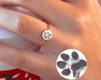 May include: A gold ring with a paw print design. The ring is on a person's finger. A black and white paw print sticker is on the person's hand.