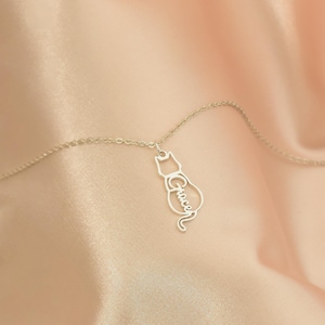 May include: A silver necklace with a cat-shaped pendant. The pendant is cut out and the name "Grace" is written inside the cat's body.