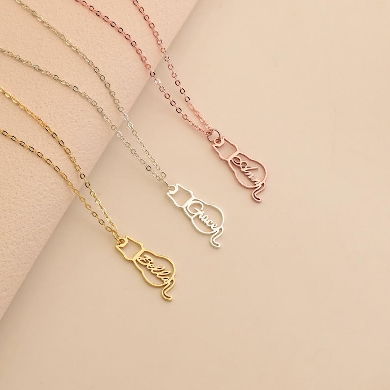May include: Three gold, silver, and rose gold necklaces with cat-shaped pendants. Each pendant has a name inscribed in cursive: "Gracen", "Allison", and "Anya".