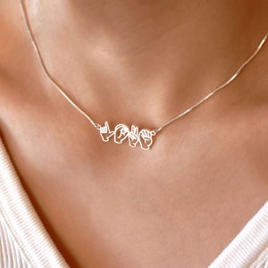 Può includere: Una collana d'argento con un ciondolo che scrive "LOVE" nel linguaggio dei segni americano.
