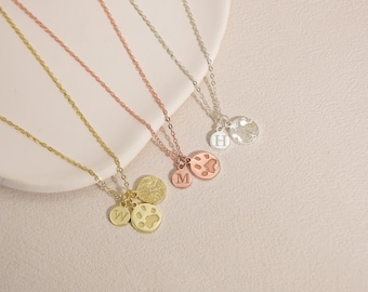 Puede incluir: Cuatro delicados collares con colgantes. Un collar dorado tiene un dije de huella de pata y un dije con la letra "W". Un collar de oro rosa tiene un dije de huella de pata y un dije con la letra "M". Un collar plateado tiene un dije con la letra "H" y un dije texturizado.