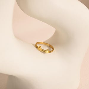 May include: A gold ring featuring a cat ear design. The ring is inscribed with the word "Belle". The ring is placed on a white surface.