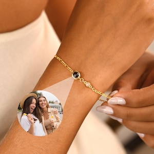 May include: A gold-colored bracelet with a small black stone and two clear stones. The bracelet is on a person's wrist. A small inset image shows two women.