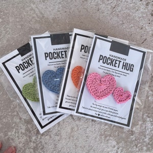 May include: Three handmade crocheted heart-shaped pocket hug gifts. Each gift comes with a card that reads "Handmade Pocket Hug" and includes a message about the hearts. The hearts are in green, blue, and pink.