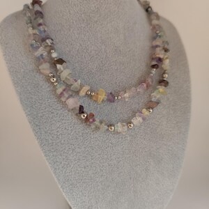 Op de afbeelding: Een veelkleurige edelsteenketting met zilveren kralen. De ketting is gemaakt van verschillende tinten paarse, blauwe, groene en roze edelstenen.