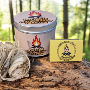 May include: A portable marshmallow toaster kit, including a tin with a silver lid and the text "Portable Marshmallow Toaster". A box of campfire matches and a bundle of fire starter are also present. The background is a blurred forest scene.