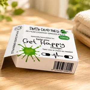May include: A white rectangular box labeled Drop Dead Fred containing 28 film coated green pills. The packaging features a green ink splatter graphic, the text Get Happy, a 10mg dosage indicator, a heartbeat line icon, and a barcode at the bottom.