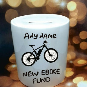 Może przedstawiać: Biała ceramiczna skarbonka z czarną sylwetką roweru elektrycznego i tekstem "Any name NEW EBIKE FUND".