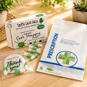 May include: A white box labeled Drop Dead Fred 28 film coated green pills 10mg with text help you Get Happy, a white prescription paper bag with a green cross, a clear plastic bag with Thank you text, and several white and green capsules.