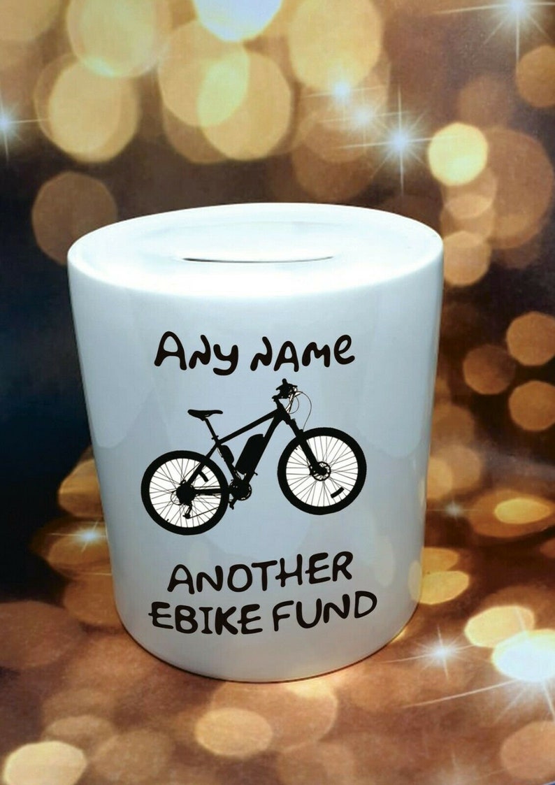 Może przedstawiać: Biała ceramiczna skarbonka z czarną sylwetką roweru elektrycznego i tekstem "Any name Another Ebike Fund".