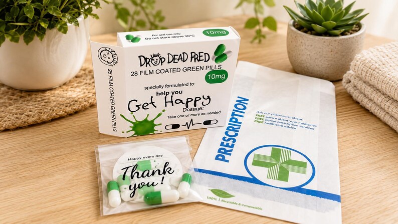 May include: A white rectangular box labeled Drop Dead Fred 28 film coated green pills 10mg with a green splash graphic, a small clear plastic bag containing green and white capsules with a Thank You tag, and a white prescription paper bag.