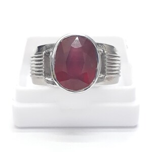 Può includere: Un anello d'argento con una grande pietra preziosa di rubino di forma ovale. L'anello ha una fascia testurizzata.