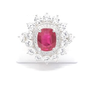 Peut inclure: Une bague en argent avec un gros rubis de forme ovale entouré d'un halo de petits diamants ronds.