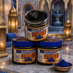 Peut inclure: Trois pots cylindriques de savon noir avec des couvercles bleus, empilés avec un pot ouvert au sommet. Les étiquettes portent le texte Savon Noir a Nila Sahraouia et une image de poudre bleue. Un petit bol de poudre bleue est au premier plan.
